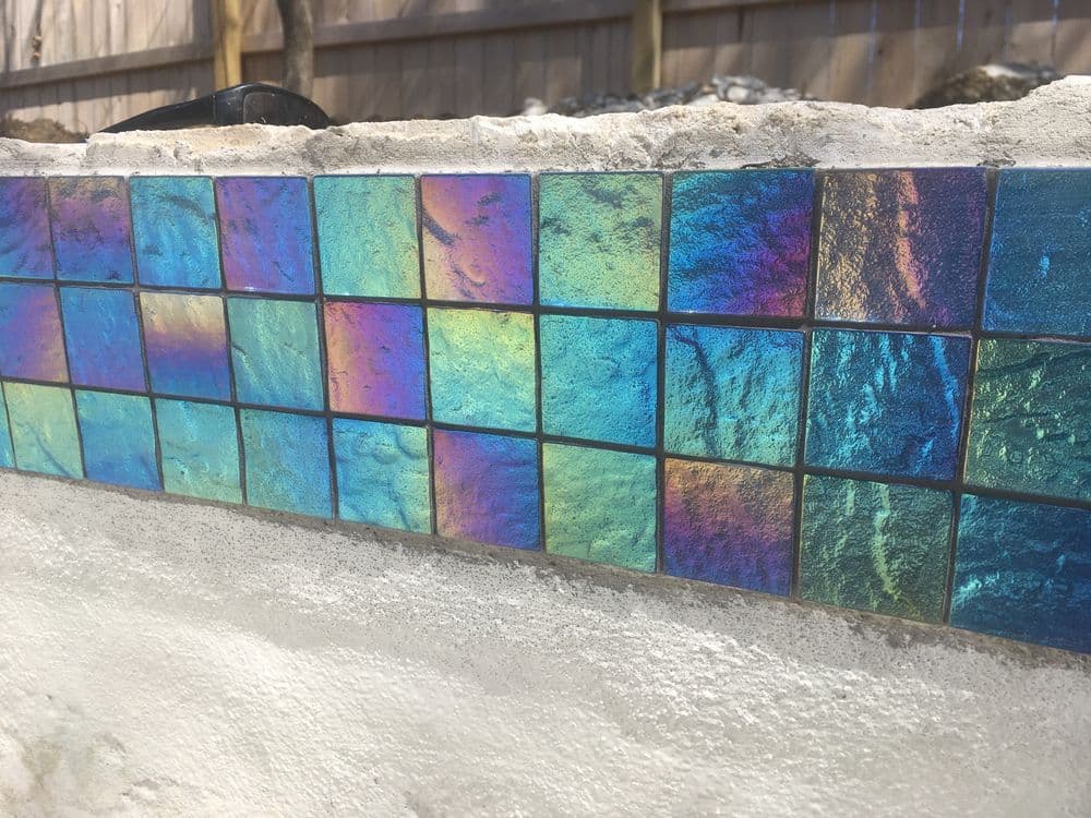Iridescent tile mosaic on a wall, showcasing vibrant colors and reflections.