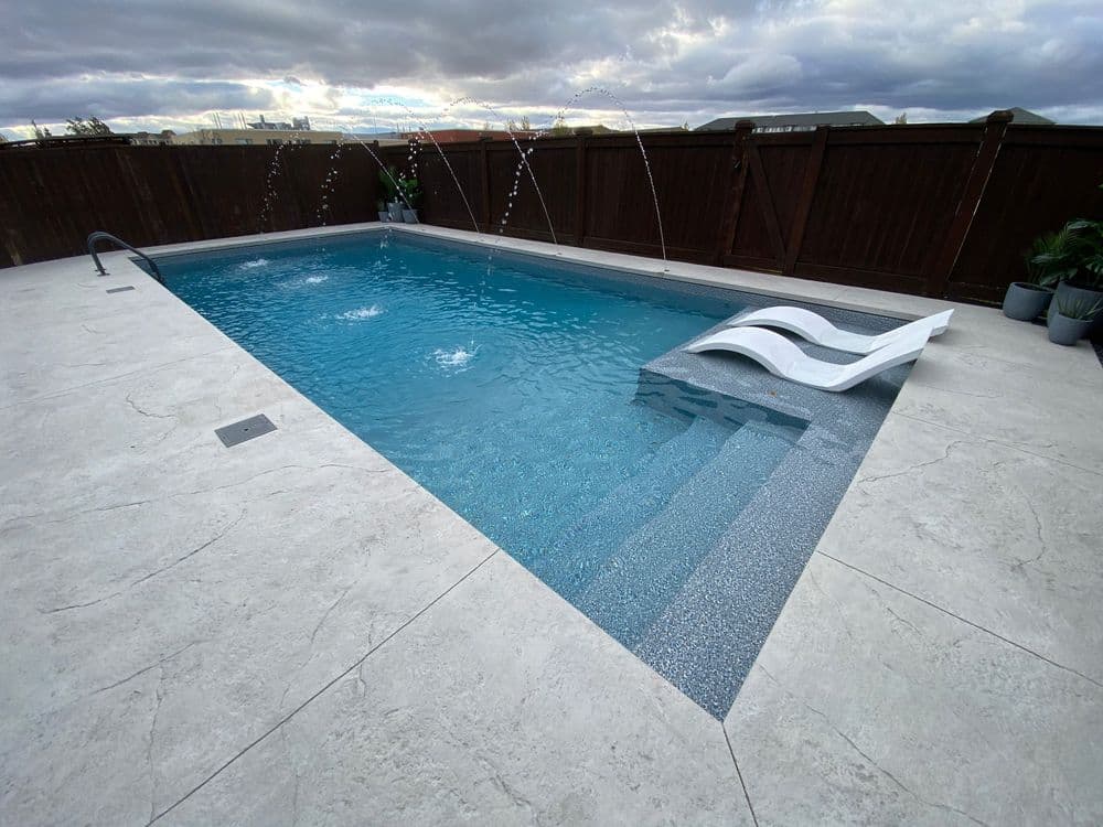 Modern backyard swimming pool with water features, surrounded by stylish stone decking.